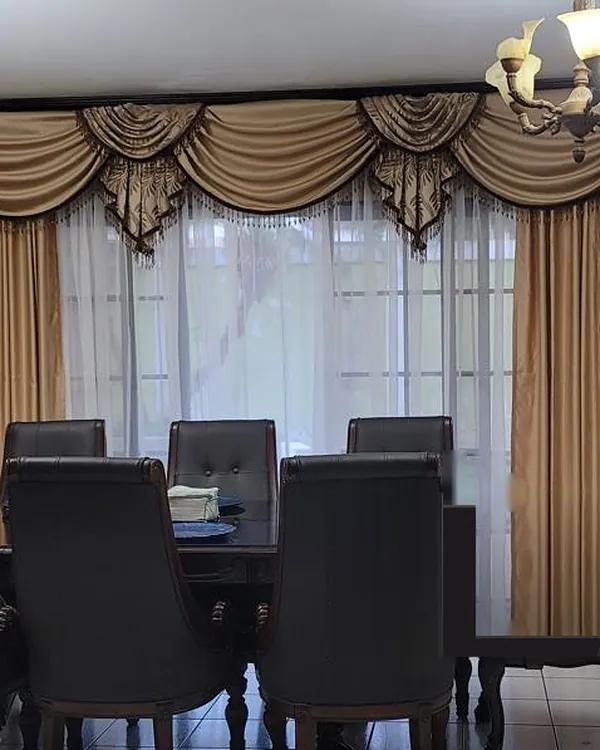 Balance de satín dorado con ondas y picos con flecos de cuentas, cascadas de tela con hojas y cortinas doradas a los lados de un velo blanco, en un comedor