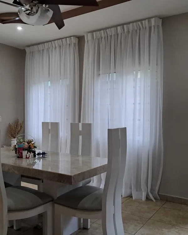 Cortinas de velo blanco con paletón, de suelo a techo, en las ventanas de un comedor con sillas blancas